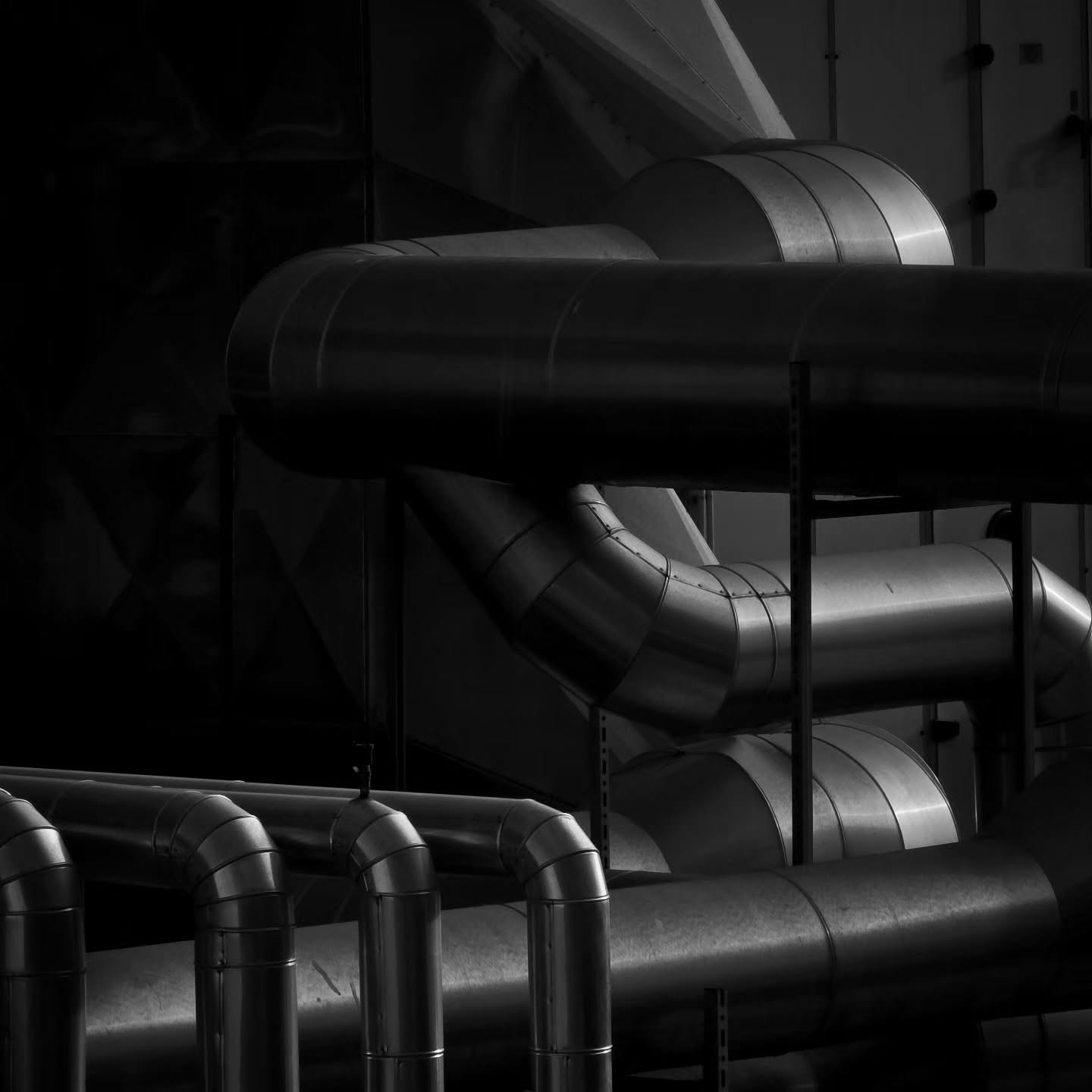 Curving metal ducts catch a sliver of light in a dark industrial space.